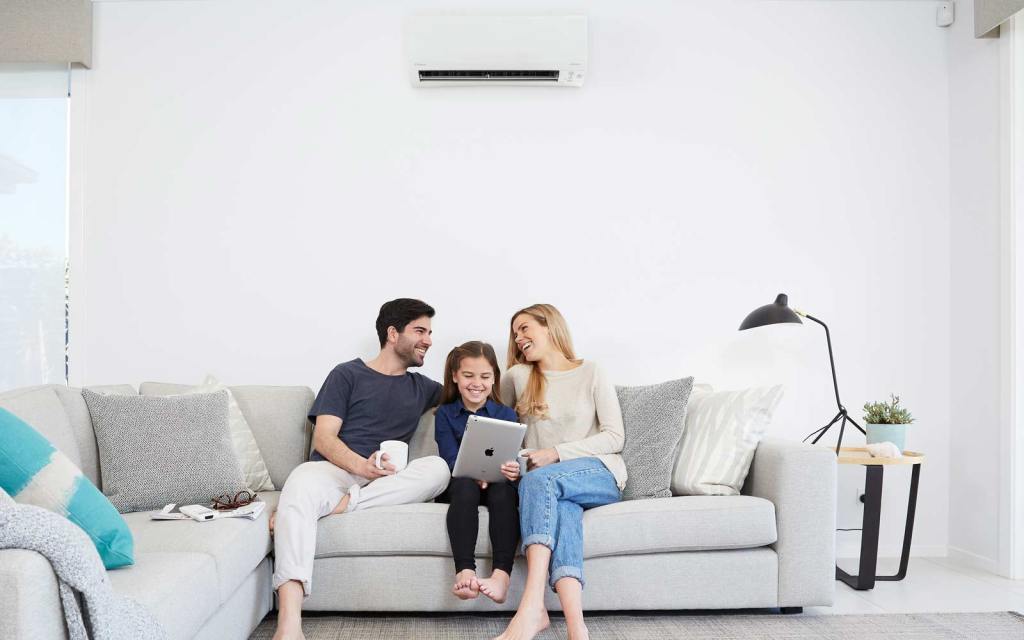 Mother, Father and Daughter Sitting on Couch in Family Room Looking at iPad - Peninsula Air Conditioning